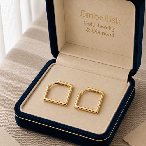 Gold earrings in a 'Embellish' jewelry box on a beige surface