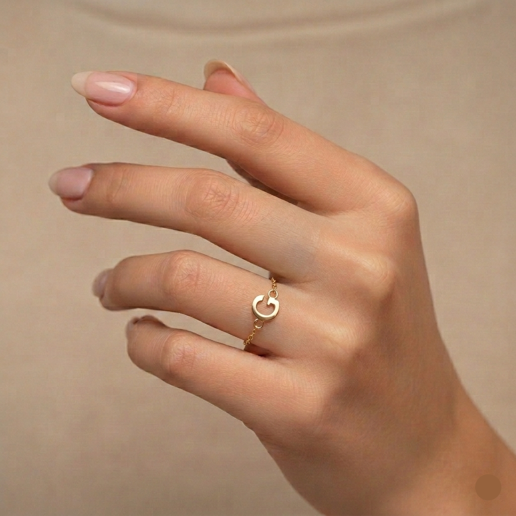 Hand wearing a gold ring with a 'C' on a beige background