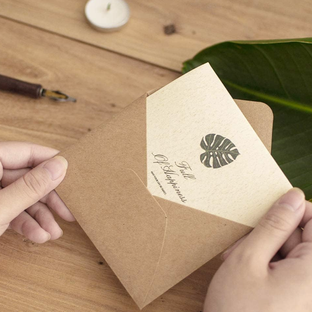 Person holding a brown envelope with a leaf design on a wooden surface