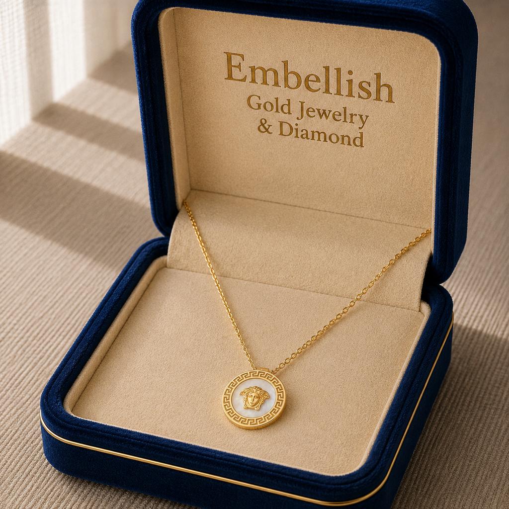 Gold necklace with a pendant in an 'Embellish' jewelry box on a beige surface.