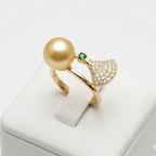 Gold ring with a large pearl and green gemstone on a white stand