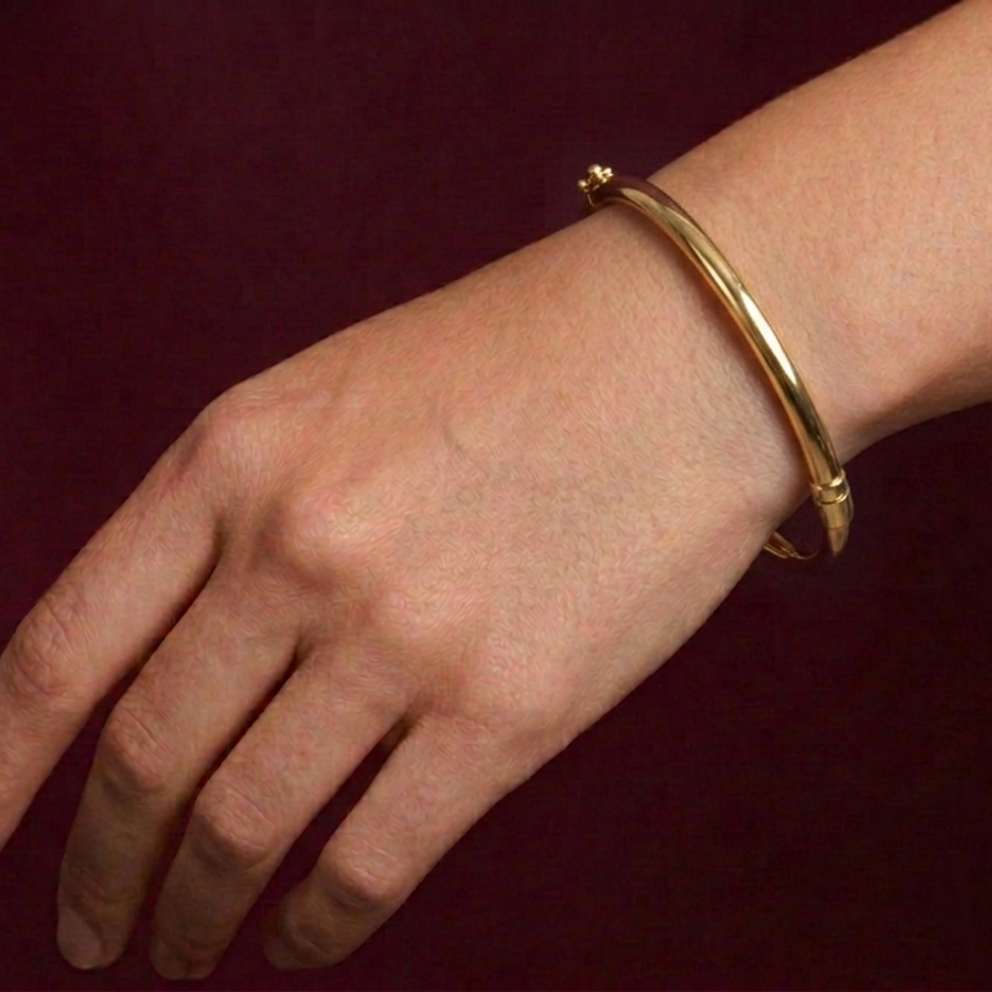 Gold bracelet on a wrist against a dark background
