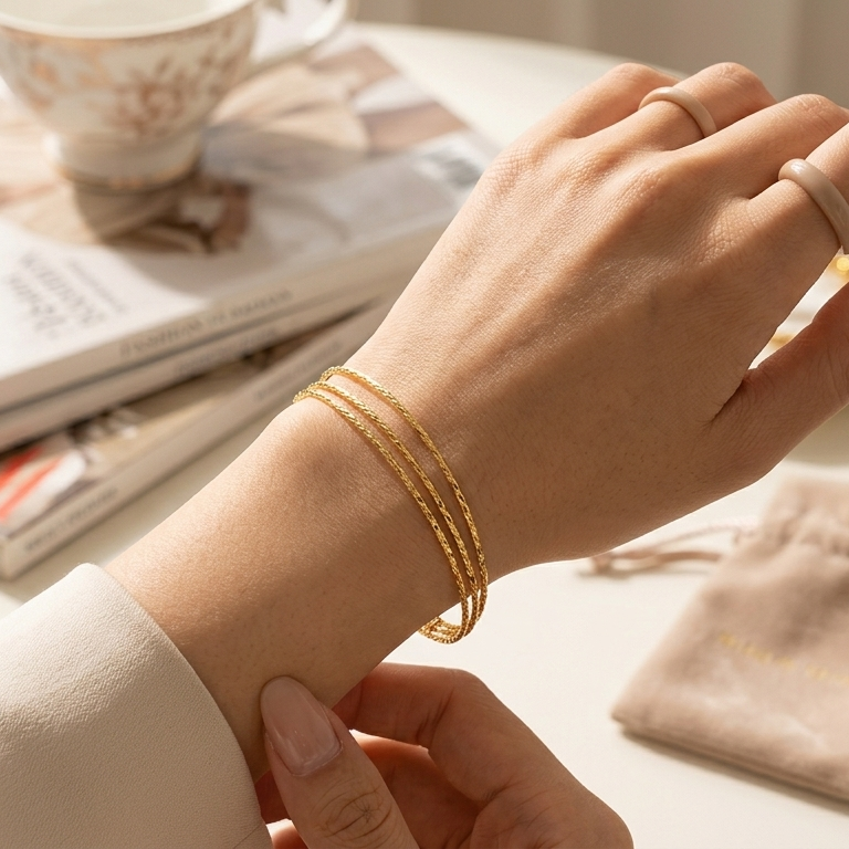 Hand wearing a gold bracelet with a magazine and pouch in the background