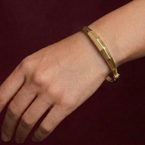 Gold bracelet on a wrist against a dark red background