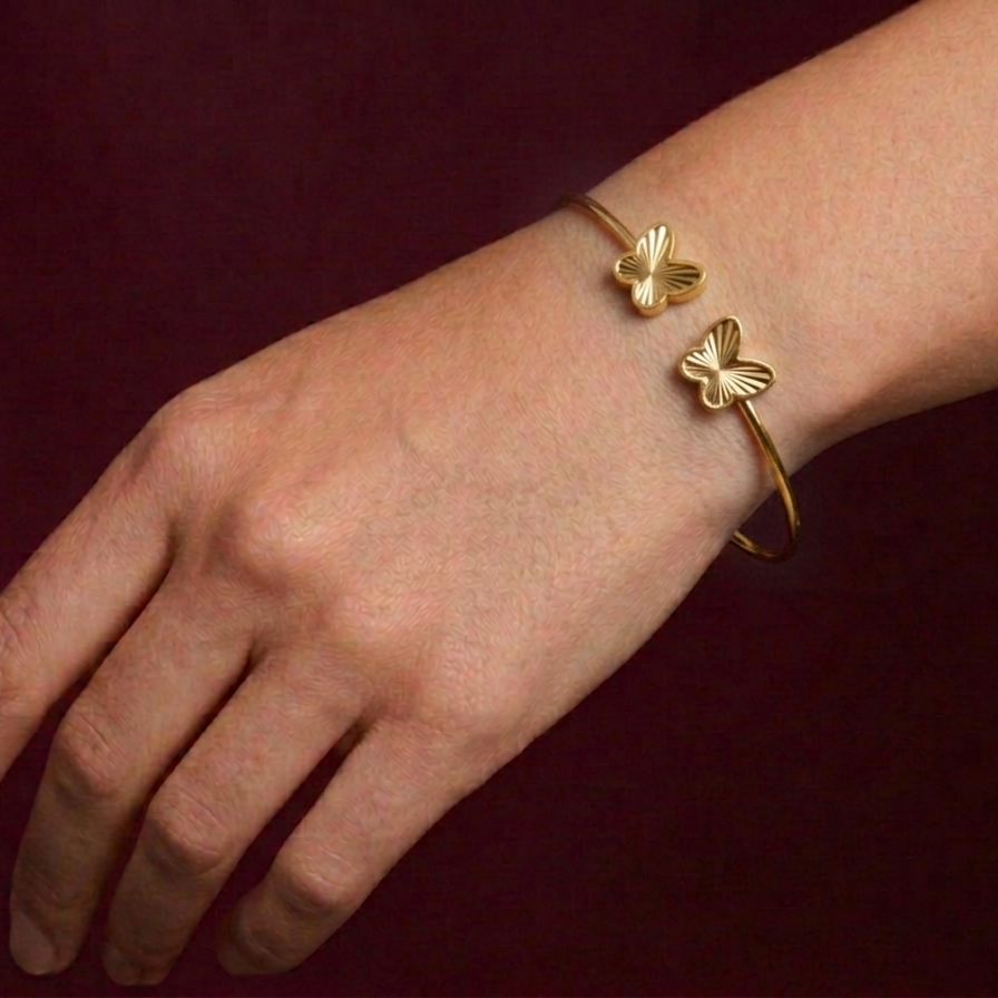 Gold bracelet with butterfly designs on a wrist against a dark background