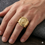 Gold ring with a detailed design on a person's finger against a dark background