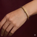 Gold bracelet on a wrist against a dark red background