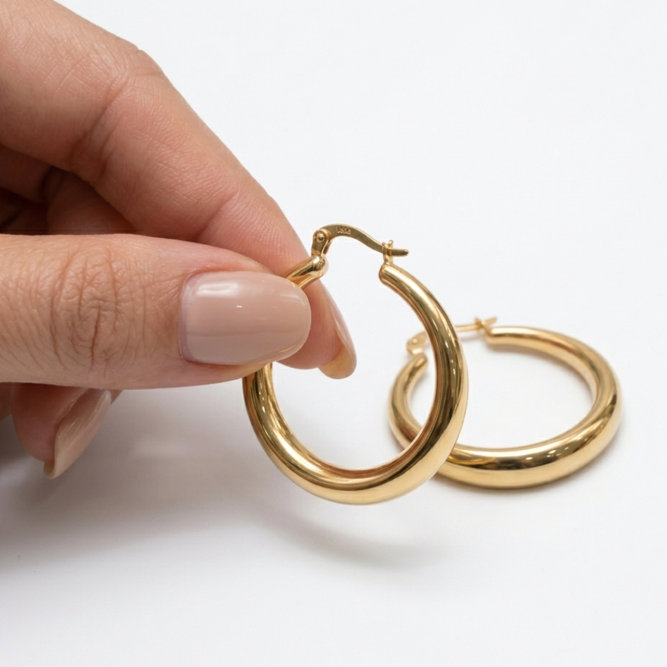 Gold hoop earrings held by a hand on a white background