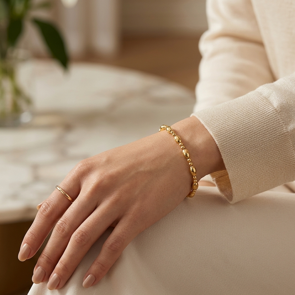 Hand wearing a gold bracelet on a neutral background