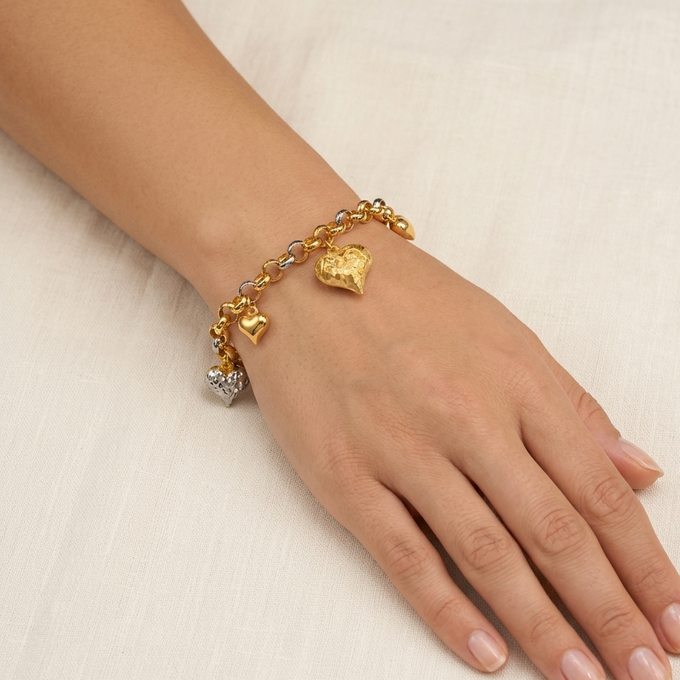 Gold bracelet with heart charms on a hand against a beige background