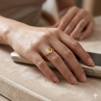 Hand wearing a gold ring on a beige surface with a blurred background