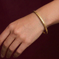 Gold bracelet on a wrist against a dark background