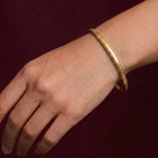 Gold bracelet on a wrist against a dark background