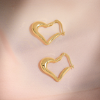 Gold heart-shaped hoop earrings on a pink satin background