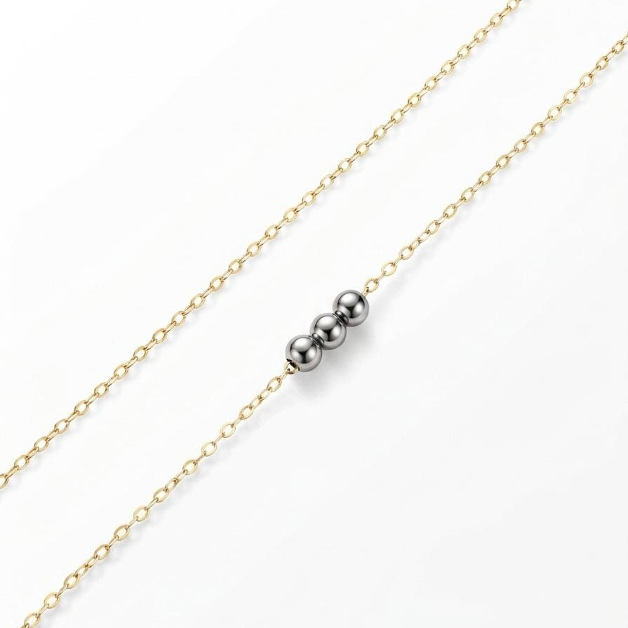 Gold chain necklace with a silver bead on a white background