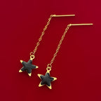 Gold chain earrings with black star charms on red background, elegant jewelry design