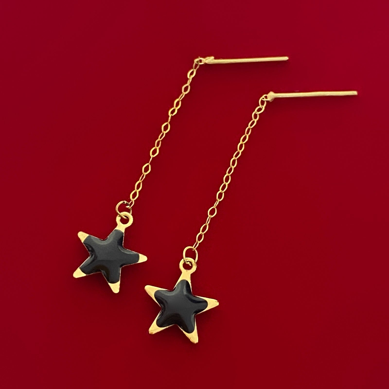 Gold chain earrings with black star charms on red background, elegant jewelry design