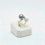 Gold ring with a large gray pearl on a white stand against a light gray background