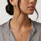 Close-up of a woman wearing a gold necklace with a pendant against a neutral background