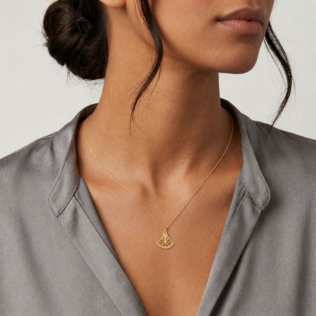 Woman wearing a gold necklace with a geometric pendant against a neutral background