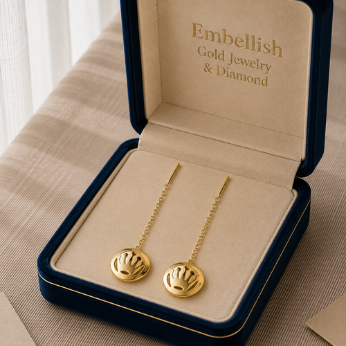 Gold earrings in a 'Embellish Gold Jewelry & Diamond' box on a beige surface.