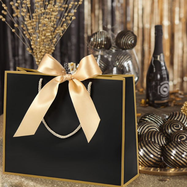 Black gift bag with a gold ribbon on a festive background with decorative items.