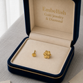 Gold earrings in a 'Embellish Gold Jewelry & Diamond' box on a gray surface.