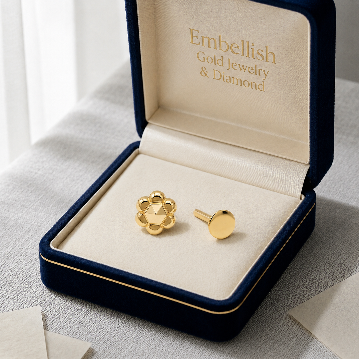 Gold earrings in a 'Embellish Gold Jewelry & Diamond' box on a light gray surface.