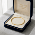 Gold bracelet in a 'Embellish Gold Jewelry & Diamond' box on a gray surface